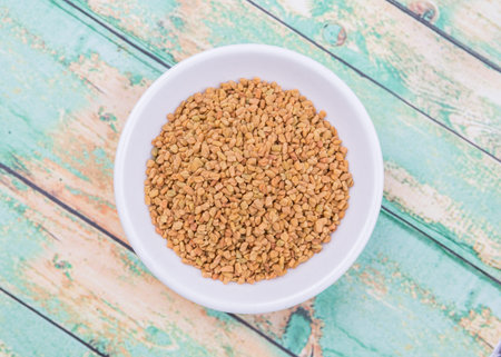 Fenugreek seeds in white bowl over wooden background