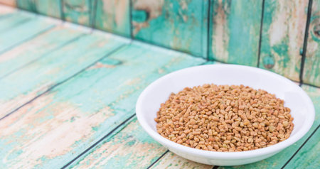 Fenugreek seeds in white bowl over wooden backgroundの写真素材