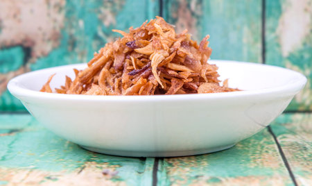 Deep fried shallots for garnishing in white bowl over wooden background