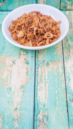 Deep fried shallots for garnishing in white bowl over wooden backgroundの写真素材