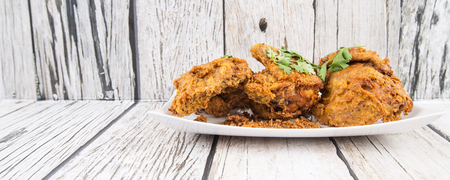 Popular Javanese dish Ayam Penyet or crispy fried chicken in a white plate over wooden backgroundの写真素材
