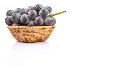 A bunch of black grapes in a wicker bowl over white backgroundの写真素材