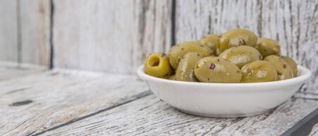 Pickled olive in a white bowl over wooden backgroundの写真素材