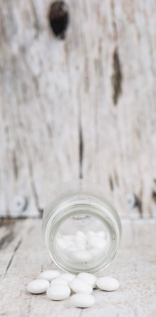 Medicinal pills in a glass bottle over wooden backgroundの写真素材