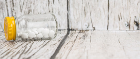 Medicinal pills in a glass bottle over wooden backgroundの写真素材