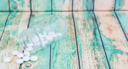 Medicinal pills in a glass bottle over wooden backgroundの写真素材