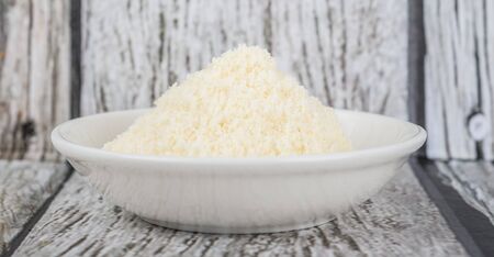 Grated cheese in white bowl over wooden backgroundの写真素材