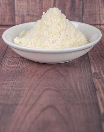 Grated cheese in white bowl over wooden backgroundの写真素材