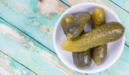 Dill pickles in a white bowl over wooden background