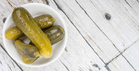 Dill pickles in a white bowl over wooden backgroundの写真素材