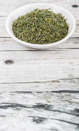 Dried green tea leaves in white bowl over wooden backgroundの写真素材