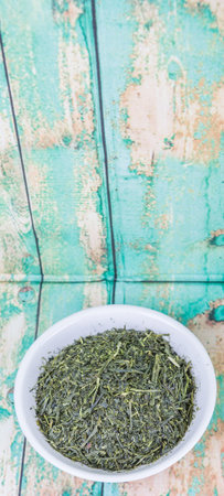 Dried green tea leaves in white bowl over wooden backgroundの写真素材