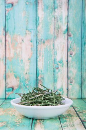 Fresh rosemary herbs over in white bowl over wooden backgroundの写真素材