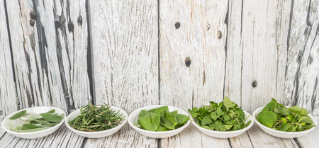 Rosemary, mint, parsley and sage leaves herbs in white bowl over wooden background