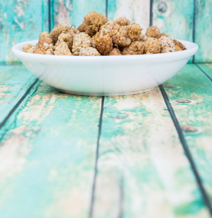 Dried white mulberry in white bowl over wooden backgroundの写真素材