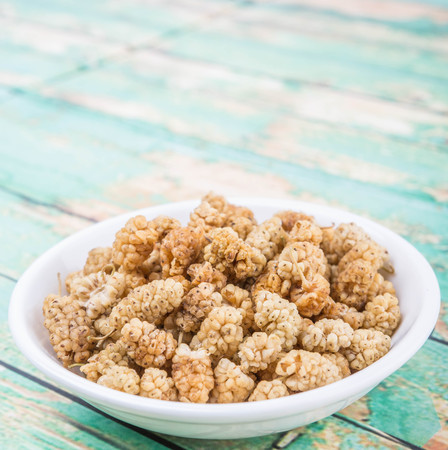 Dried white mulberry in white bowl over wooden backgroundの写真素材