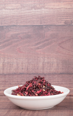 Dried red hibiscus tea leaves in white bowl over wooden backgroundの写真素材