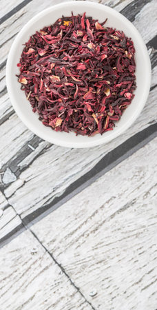 Dried red hibiscus tea leaves in white bowl over wooden backgroundの写真素材