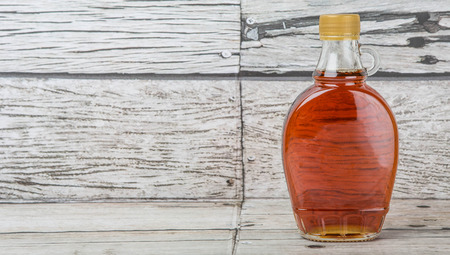 Maple syrup in a glass bottle over wooden backgroundの写真素材