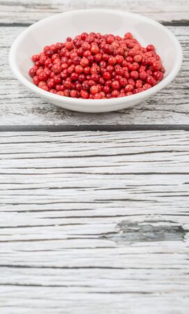 Pink peppercorn in a white bowl over wooden backgroundの写真素材