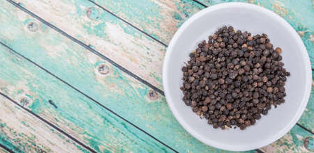 Black peppercorn in white bowl over wooden backgroundの写真素材