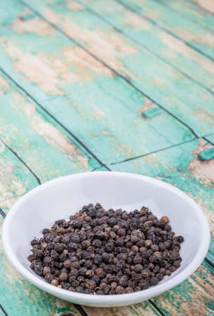Black peppercorn in white bowl over wooden backgroundの写真素材