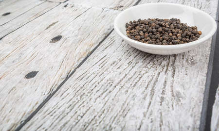 Black peppercorn in white bowl over wooden backgroundの写真素材