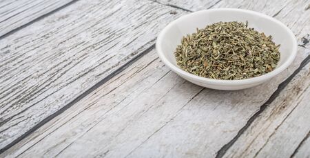 Dried lemon balm leaves in white bowl over wooden backgroundの写真素材