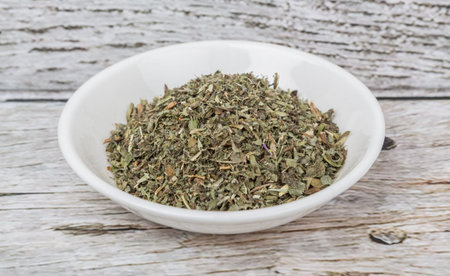 Dried lemon balm leaves in white bowl over wooden background
