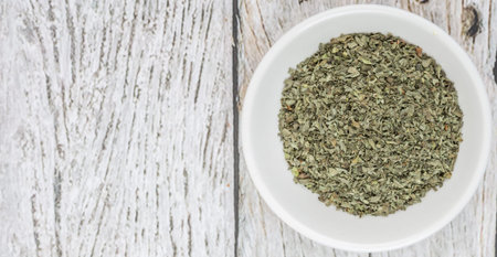 Dried basil leaves herbs over in white bowl over wooden background
