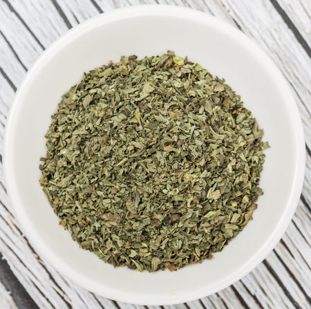 Dried basil leaves herbs over in white bowl over wooden backgroundの写真素材