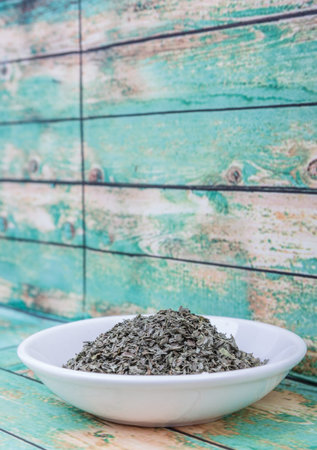 Dried basil leaves herbs over in white bowl over wooden backgroundの写真素材