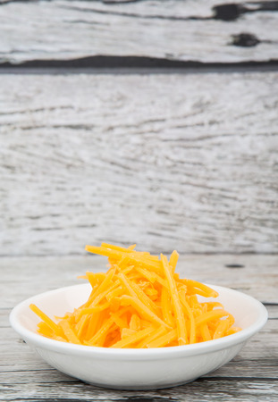 Grated cheddar cheese in white bowl over wooden backgroundの写真素材