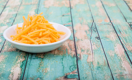 Grated cheddar cheese in white bowl over wooden background