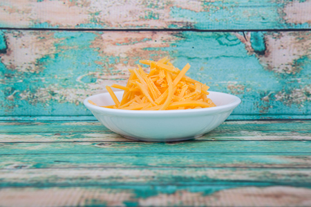 Grated cheddar cheese in white bowl over wooden bacckgroundの写真素材