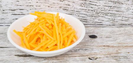 Grated cheddar cheese in white bowl over wooden bacckground