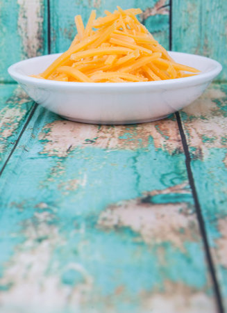 Grated cheddar cheese in white bowl over wooden bacckground