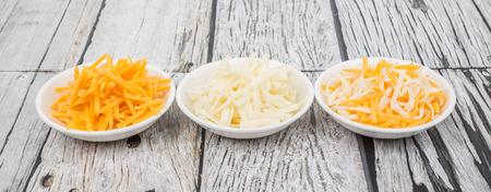 Grated cheddar and mozzarella cheese in white bowl over wooden backgroundの写真素材