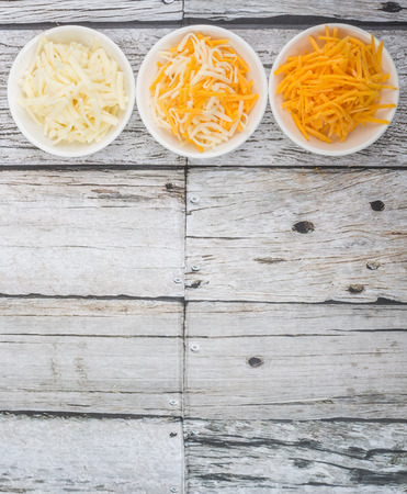 Grated cheddar and mozzarella cheese in white bowl over wooden backgroundの写真素材