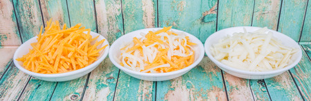 Grated cheddar and mozzarella cheese in white bowl over wooden backgroundの写真素材