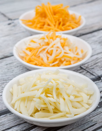 Grated cheddar and mozzarella cheese in white bowl over wooden background