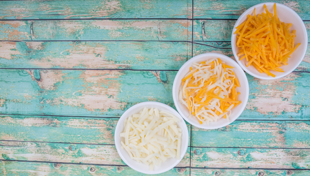 Grated cheddar and mozzarella cheese in white bowl over wooden backgroundの写真素材