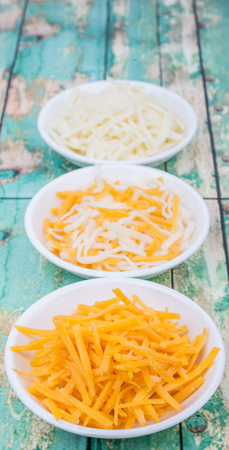 Grated cheddar and mozzarella cheese over wooden backgroundの写真素材