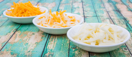 Grated cheddar and mozzarella cheese over wooden backgroundの写真素材