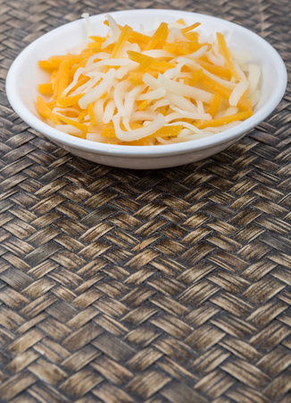 Grated cheddar and mozzarella cheese over in white bowl over wicker backgroundの写真素材