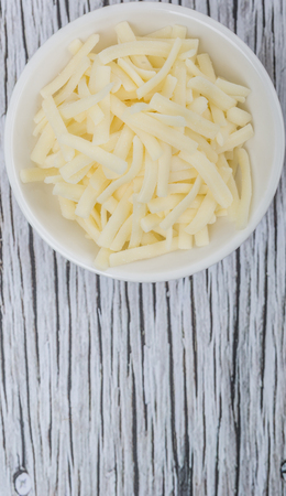 Grated mozzarella cheese in white bowl over wooden backgroundの写真素材