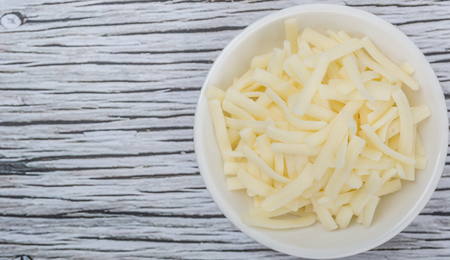 Grated mozzarella cheese in white bowl over wooden backgroundの写真素材