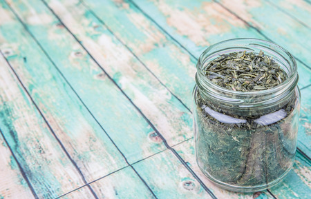 Dried Japanese green tea leaves in a mason jar over wooden backgroundの写真素材