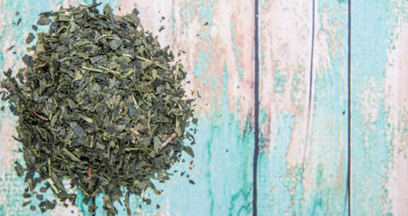 Dried Japanese green tea leaves over wooden background