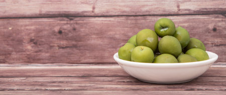 Pickled green olive in white bowl over wooden backgroundの写真素材